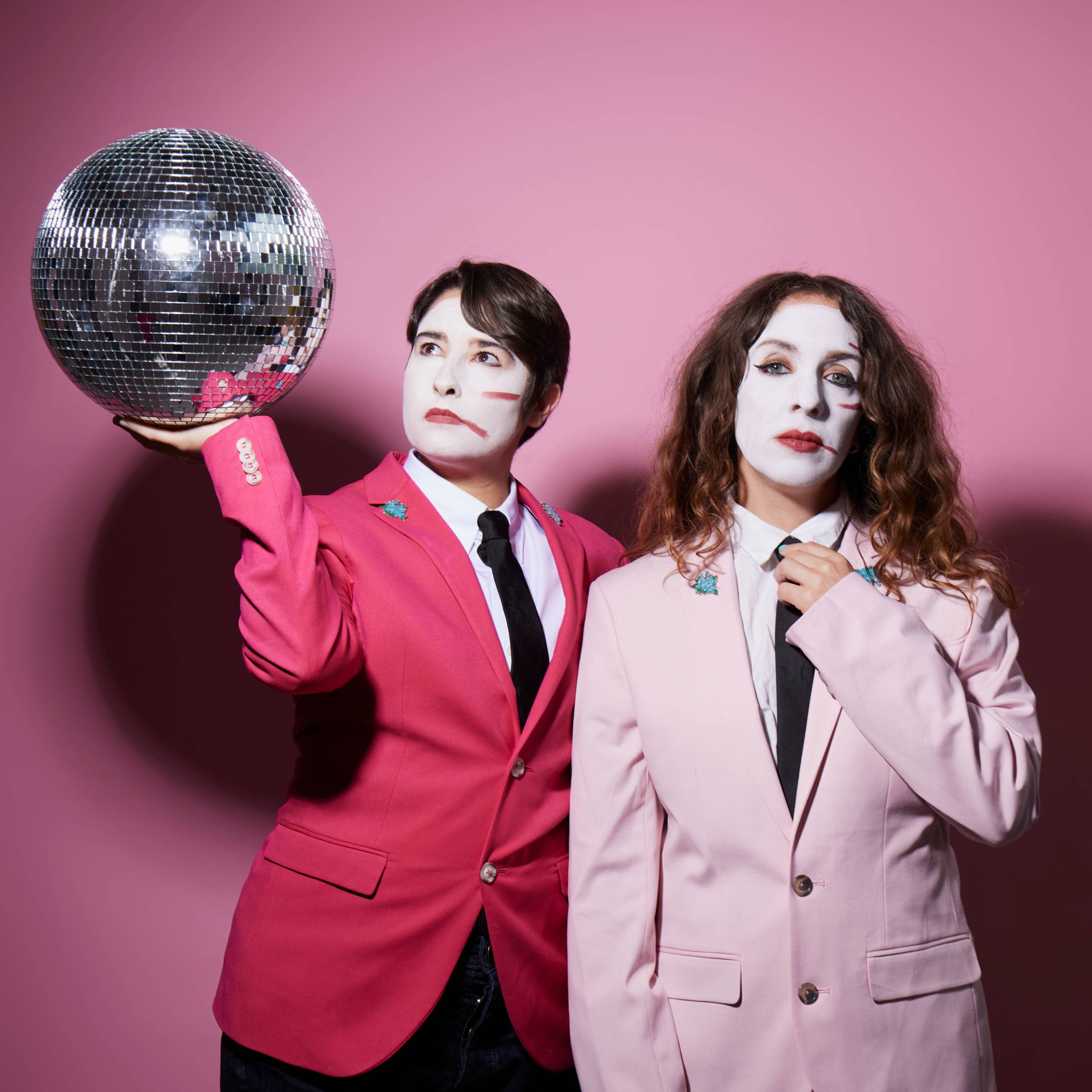 two women in white face paint and pink jackets with a disco ball