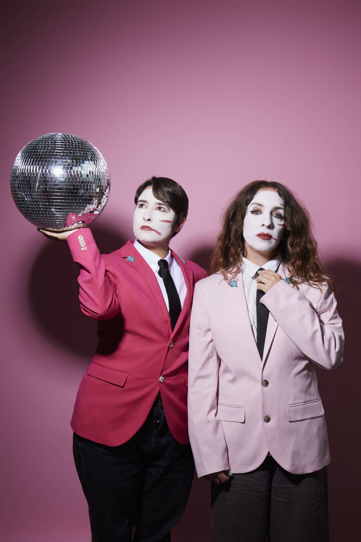two women in white face paint and pink jackets with a disco ball