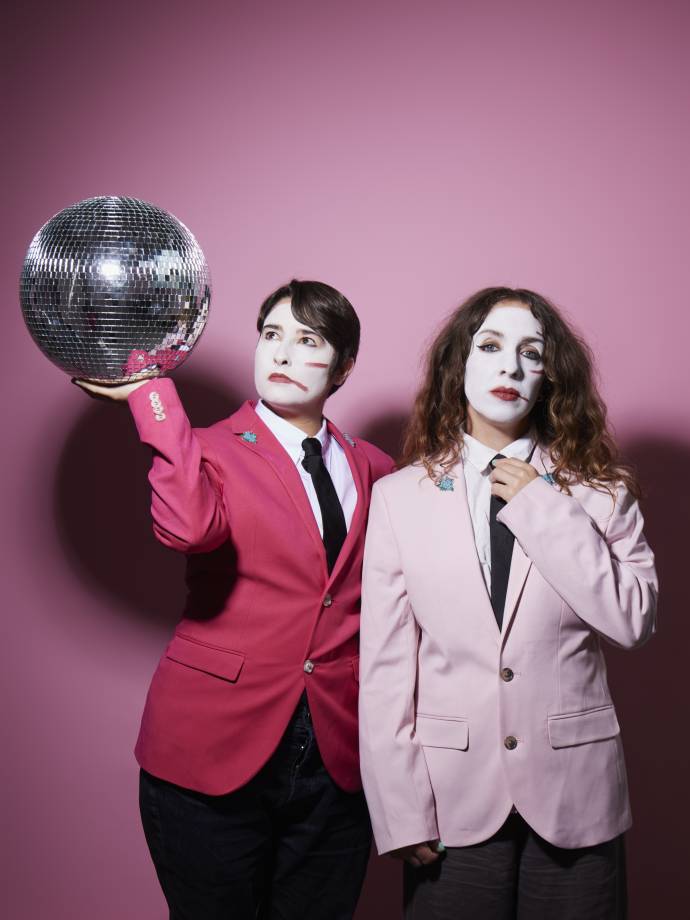 two women in white face paint and pink jackets with a disco ball